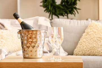Bottle of champagne in ice bucket and glasses on table in living room - obrazy, fototapety, plakaty