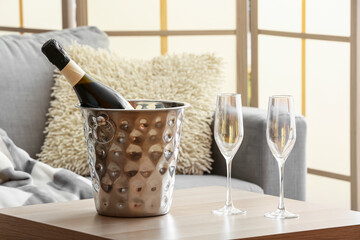 Bottle of champagne in ice bucket and glasses on table near sofa in living room