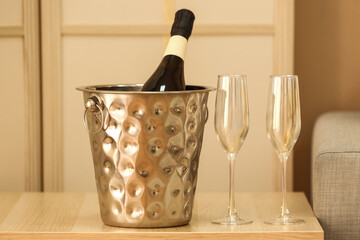 Bottle of champagne in ice bucket and glasses on table, closeup