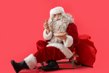 Santa Claus with tasty cookies sitting on sledges against color background