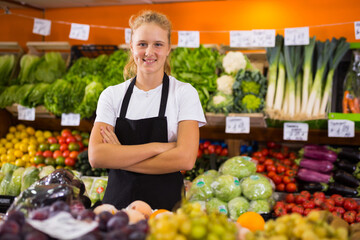 Portrait of a smiling fifteen-year-old girl who works part-time in a store as a trainee saleswoman standing near the counter ..in the vegetable department