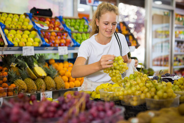 Positive european teen shopper chooses fresh grape at grocery store