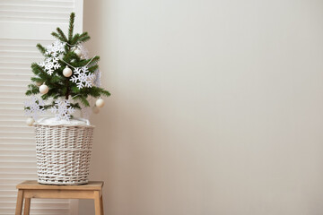 Beautiful Christmas tree in basket decorated with snowflakes and balls on table near light wall