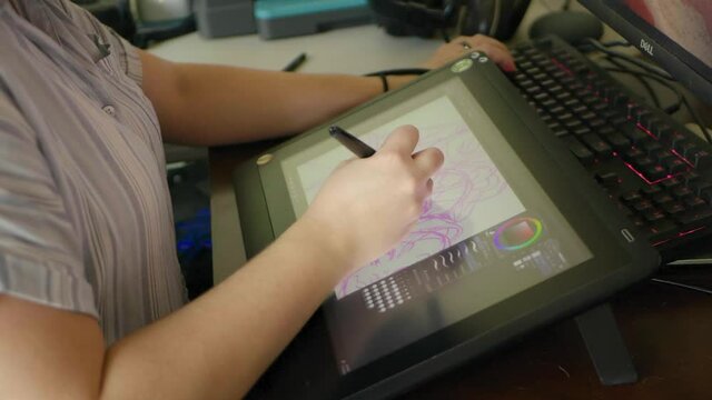 A caucasian woman's hand draws a digital illustration on a tablet in slow motion.