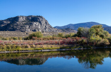 Fototapeta premium Mountains and trees reflecting in the canal in Osoyoos, BC
