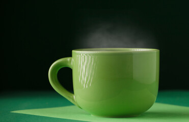Cup of green tea or coffee, hot with steam, dark green background.