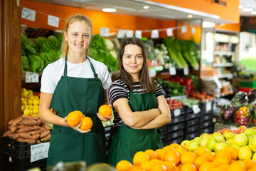 Two smiling women sellers in uniform posing at grocery section of supermarket