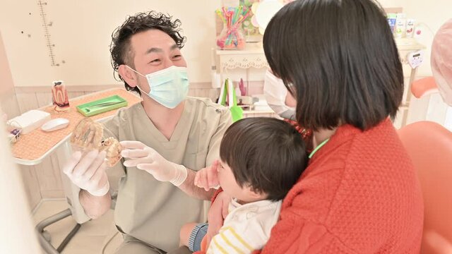 模型を使って子供の患者の指しゃぶりの説明する小児歯科医