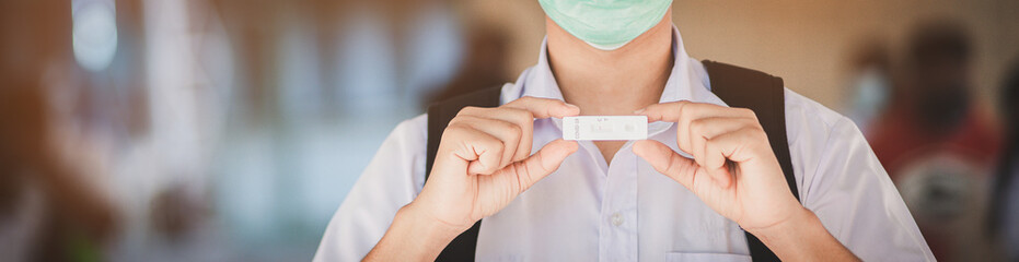 A male student in uniform carries an ATK tester for COVID-19 with negative results