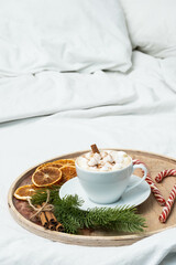 Coffee cup with marshmallow, candy cane, Christmas decorations on the bed. Winter holiday mood. Christmas morning, coffee time.