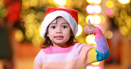 New year anticipation.The cute little girl Wearing a red Christmas hat and beautiful color shirt on a christmas background with bokeh lights .Have fun and have fun during this important season.