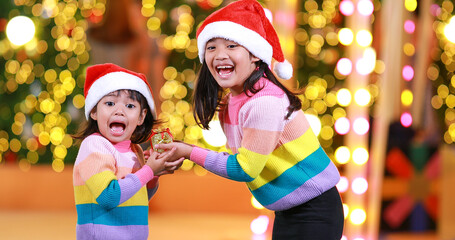 New year anticipation.Two cute little girl Wearing a red Christmas hat and beautiful color shirt on a christmas background with bokeh lights .Have fun and have fun during this important season.