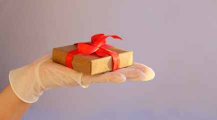 Hands in medical gloves, give a gift box with a red ribbon.