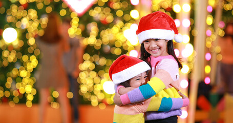 New year anticipation.Two cute little girl Wearing a red Christmas hat and beautiful color shirt on a christmas background with bokeh lights .Have fun and have fun during this important season.