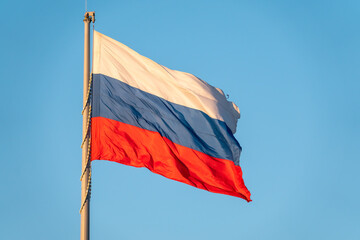 Russian tricolor flag waving in the wind against a blue sky.