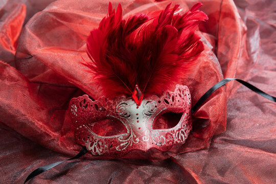 Carnival Venetian red mask with feathers on red color fabric background, female disguise, masquerade