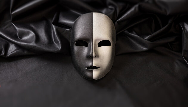 Carnival Venetian two faced mask, half black half silver on dark satin textile background,