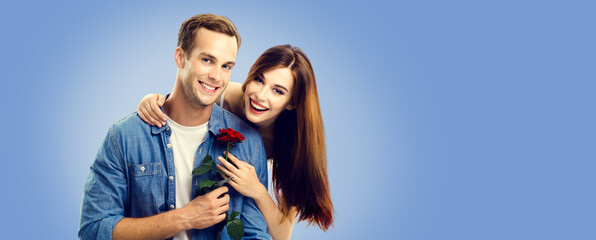 Fototapeta na wymiar Love, relationship, dating, flirting, romantic concept - portrait picture of happy couple with flower, looking at camera. Blue color background. Copy space for text. Valentines Day.