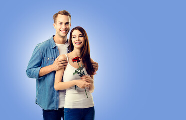 Love, relationship, dating, flirting, romantic concept - portrait of happy smiling young couple with rose flower, standing close to each other. Blue color background. Copy space.