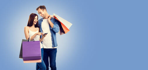 Love, holiday sales, shop, rebates, discounts offers concept - happy smiling couple with shopping bags, and cellphone, standing close to each other. Blue color background.