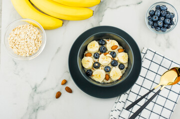 healthy homemade oatmeal porridge in a dark bowl with slices of ripe banana and blueberries. almonds to improve the vkua. top view. marble table.