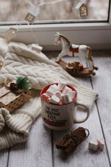 A mug with marshmallows, a white sweater, toys on a light photo background.