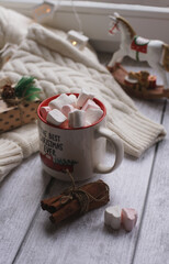 A mug with marshmallows, a white sweater, toys on a light photo background.