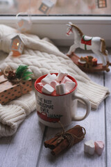 A mug with marshmallows, a white sweater, toys on a light photo background.