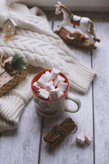 A mug with marshmallows, a white sweater, toys on a light photo background.