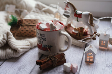 A mug with marshmallows, a white sweater, toys on a light photo background.
