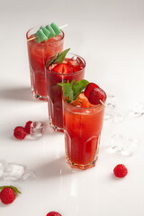Three glasses of iced berry cocktail with fruit jelly, basil and mint leaves