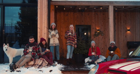 Beautiful Christmas vacation. Group of happy friends with hot drinks look at camera at winter house terrace slow motion.