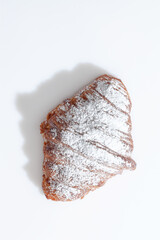 Crispy French croissant sprinkled with powdered sugar on white surface