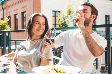 Smiling beautiful woman and her handsome boyfriend. Happy cheerful family. Couple cheering with glasses of red wine at their date in restaurant. They drinking alcohol at veranda cafe in the street