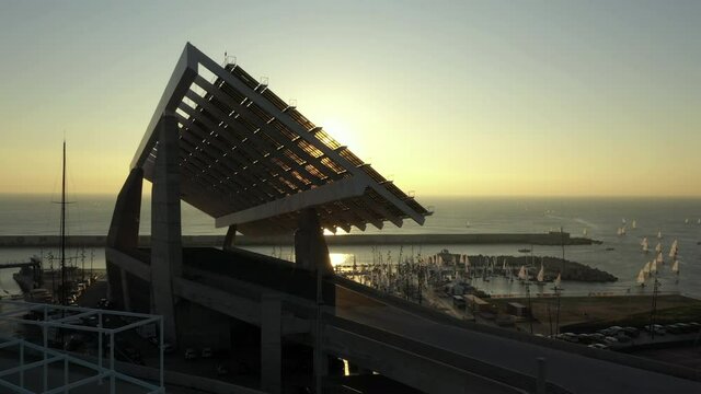 Sun emerging from behind Barcelona solar panel structure aerial rising view Parc Del Forum marina