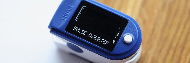 Blue pulse oximeter lying on wooden table with documents closeup