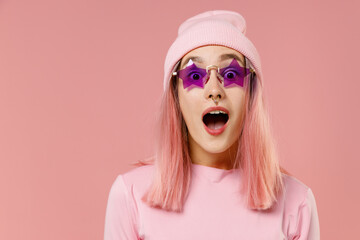 Young shocked caucasian woman 20s with bright dyed rose hair in rosy top shirt hat glasses look camera isolated on plain light pastel pink background studio portrait. People lifestyle fashion concept.
