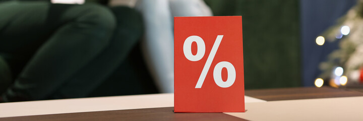 Red card with percent standing on table in store against background of customers closeup