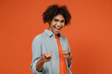 Young cheerful smiling confident student black man 50s wearing blue shirt t-shirt point index finger camera on you isolated on plain orange color background studio portrait. People lifestyle concept.