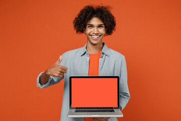 Young student black man 50s in blue shirt t-shirt hold use work on laptop pc computer with blank screen workspace area show thumb up isolated on plain orange color background People lifestyle concept