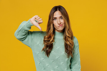 Young dissatisfied sad unhappy caucasian woman 30s wearing green knitted sweater showing thumb down dislike gesture isolated on plain yellow color background studio portrait. People lifestyle concept. - obrazy, fototapety, plakaty