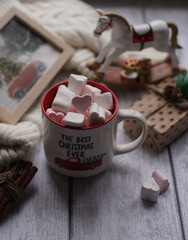 A mug with marshmallows, a white sweater, toys on a light photo background.