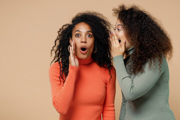 Two shocked young curly black women friends 20s wearing casual shirts clothes whispering gossip and...