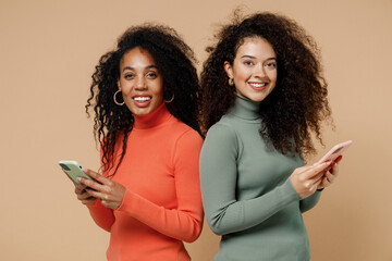 Two happy young curly black women friends 20s wearing casual shirts clothes hold in hand use mobile...