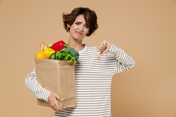 Young smiling vegetarian woman 20s in casual clothes hold paper bag with vegetables after shopping...