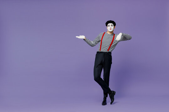 Full size body length charismatic bright young mime man with white face mask wears striped shirt beret lean on something invisible isolated on plain pastel light violet background studio portrait.