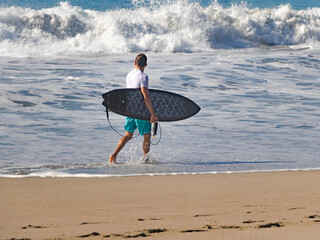 Fototapeta na wymiar Surfista mirando al horizonte mientras camina en la playa después de tomar algunas olas. 