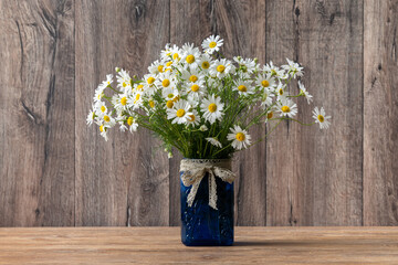 Bouquet of daisies in blue jar on dark rustic wooden background