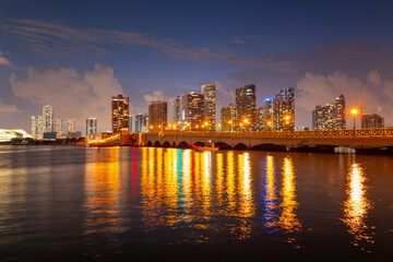 Fototapeta premium Miami, Florida cityscape skyline on Biscayne Bay. Panorama at dusk with urban skyscrapers and bridge over sea with reflection.
