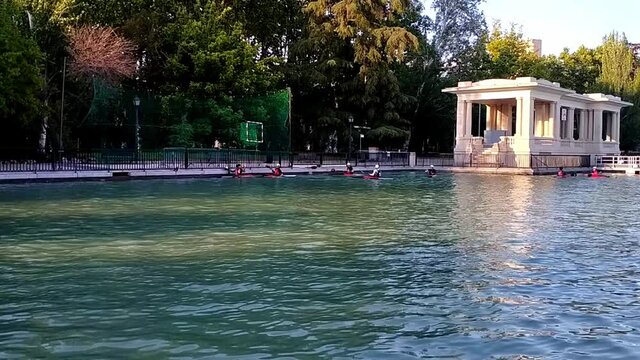 Shot of a game of kayak polo in the big pond at Retiro parl, Madrid. It's close to dusk on a sunny summer day. Kayakers pass the ball with their paddles and try to get it through the goal above them.
